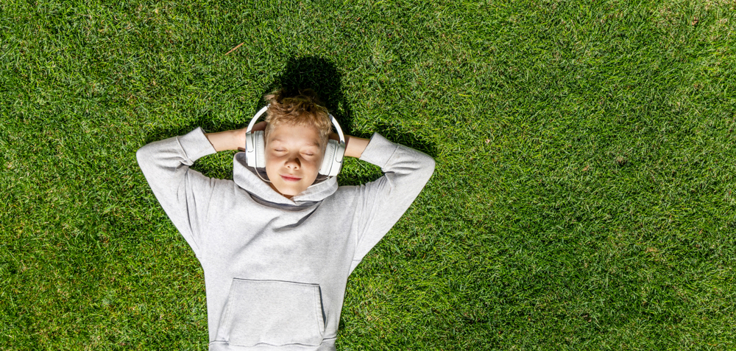 Gutt liggende i gresset med hodetelefoner