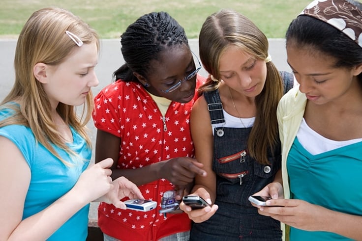 unge jenter som ser på mobiltelefonen til hverandre