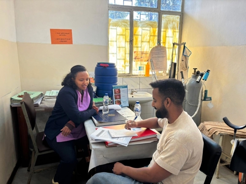 Photo of Ibrahim sitting at a desk interviewing an  in-charge working as an mother and child health coordinator